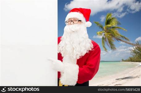 christmas holidays, advertisement, gesture, travel and people concept - man in costume of santa claus pointing finger to white blank billboard over tropical beach background