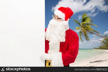 christmas, holidays, advertisement, travel and people concept - man in costume of santa claus with white blank billboard over tropical beach background