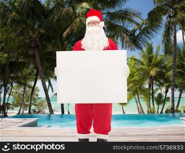 christmas, holidays, advertisement, travel and people concept - man in costume of santa claus holding white blank billboard over swimming pool on tropical beach background