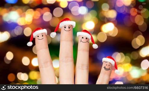 christmas, holidays and body parts concept - close up of four fingers with santa hats over festive lights background. close up of four fingers in santa hats over lights