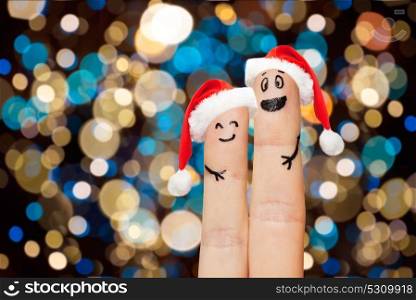 christmas, holidays and body parts concept - close up of two fingers in santa hats with smiley faces over lights background. two fingers in santa hats over christmas lights