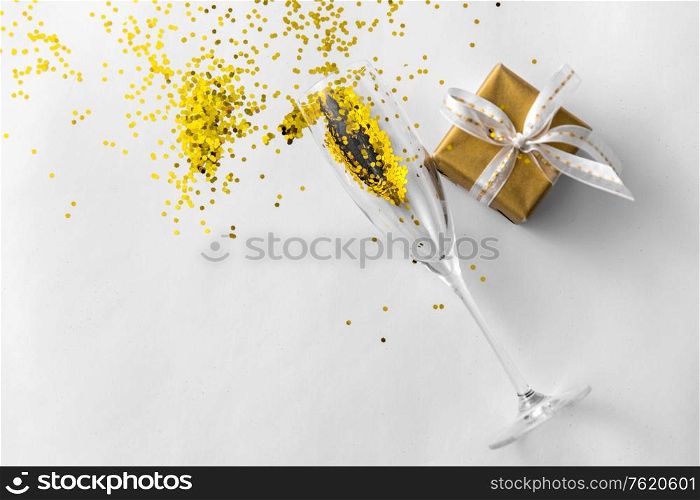 christmas, holidays and celebration concept - champagne wine glass, gift box and golden glitters on white background. champagne glass, gift and golden glitters