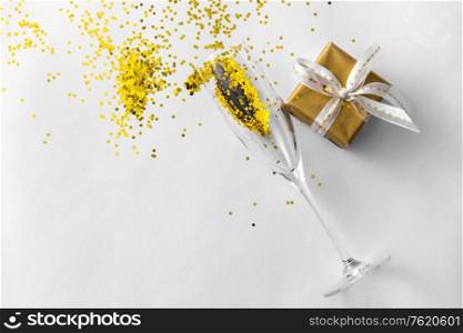 christmas, holidays and celebration concept - champagne wine glass, gift box and golden glitters on white background. champagne glass, gift and golden glitters