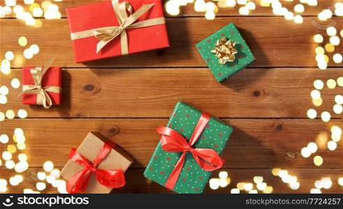 christmas, holidays and celebration concept - gift boxes on wooden boards from top over festive lights. christmas gifts on wooden boards over lights