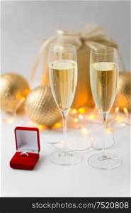 christmas, holidays and celebration concept - glasses of champagne and diamond ring in little red gift box. champagne and diamond ring in box on christmas