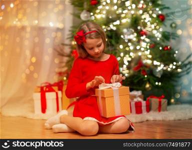 christmas, holidays and childhood concept - girl in red dress with gift box at home. girl with christmas gift at home