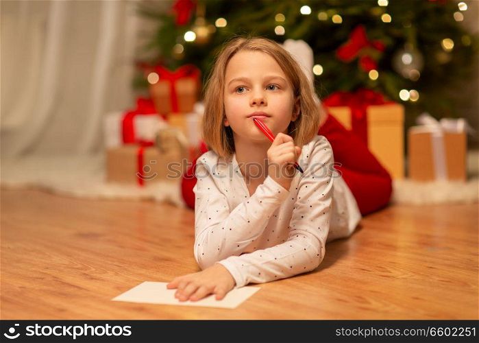 christmas, holidays and childhood concept - girl writing wish list or letter to santa at home. girl writing christmas wish list at home