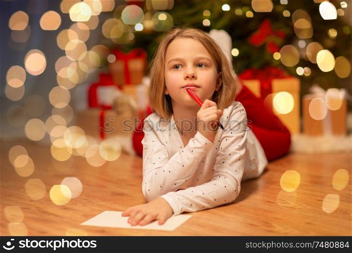 christmas, holidays and childhood concept - girl writing wish list or letter to santa at home. girl writing christmas wish list at home