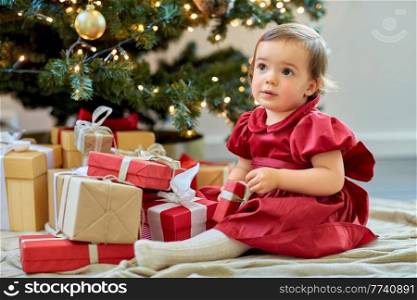 christmas, holidays and childhood concept - happy baby girl opening gifts at home. happy baby girl opening christmas gifts at home