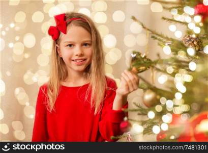 christmas, holidays and childhood concept - happy girl in red clothes decorating natural fir tree. happy girl in red decorating christmas tree