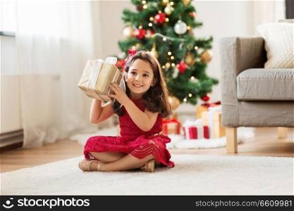 christmas, holidays and childhood concept - happy girl with gift box at home. happy girl with christmas gift at home