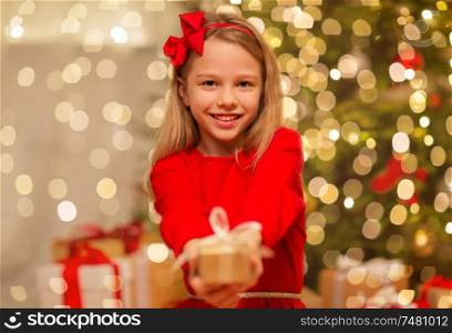 christmas, holidays and childhood concept - smiling girl in red dress with gift box at home. smiling girl with christmas gift at home