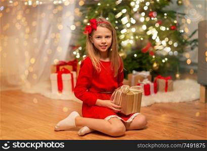 christmas, holidays and childhood concept - smiling girl in red dress with gift box at home. smiling girl with christmas gift at home