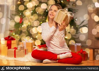 christmas, holidays and childhood concept - smiling girl with gift box at home. smiling girl with christmas gift at home