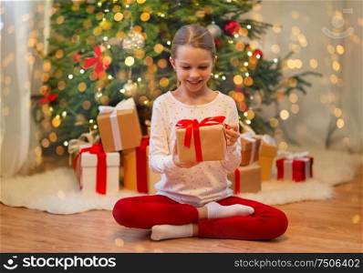 christmas, holidays and childhood concept - smiling girl with gift box at home. smiling girl with christmas gift at home