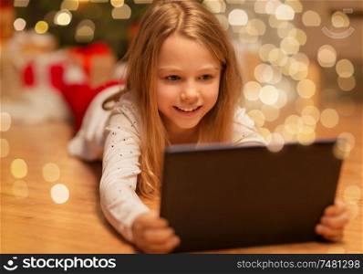 christmas, holidays and childhood concept - smiling girl with tablet pc computer at home. smiling girl with tablet pc at christmas home