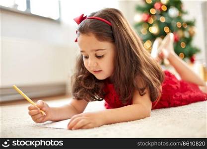 christmas, holidays and childhood concept - smiling girl writing wish list or letter to santa at home. little girl writing christmas wish list at home