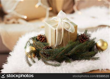 christmas, holidays and decorations concept - christmas gift and fir wreath with cones and balls at home on sheepskin. christmas gift and fir wreath with cones and balls