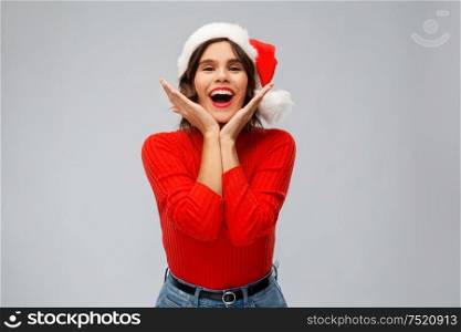 christmas, holidays and emotions concept - happy smiling young woman in santa helper hat over grey background. happy young woman in santa hat on christmas