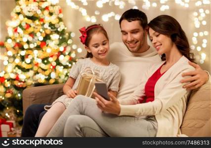 christmas, holidays and family concept - happy father, little daughter and mother with smartphone at home. family with smartphone at home on christmas