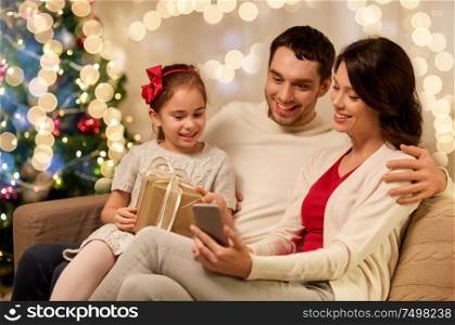 christmas, holidays and family concept - happy father, little daughter and mother with smartphone at home. family with smartphone at home on christmas