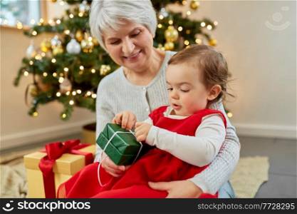 christmas, holidays and family concept - happy grandmother and baby granddaughter opening gift box at home. grandmother and baby girl with christmas gift