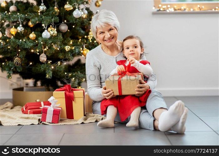 christmas, holidays and family concept - happy grandmother and baby granddaughter opening gifts at home. grandmother and baby girl with christmas gifts