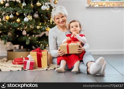 christmas, holidays and family concept - happy grandmother and baby granddaughter opening gifts at home. grandmother and baby girl with christmas gifts