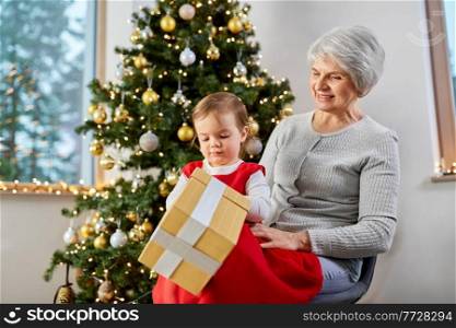 christmas, holidays and family concept - happy grandmother and baby granddaughter with gift box at home. grandmother and baby girl with christmas gift