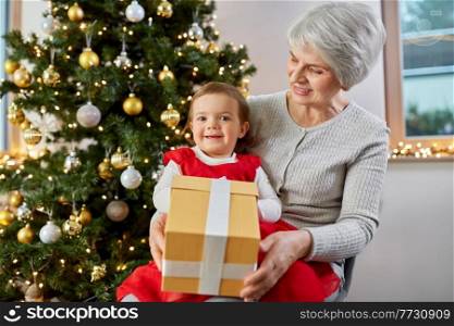christmas, holidays and family concept - happy grandmother and baby granddaughter with gift box at home. grandmother and baby girl with christmas gift