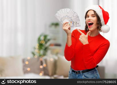 christmas, holidays and finance concept - happy smiling young woman in santa helper hat holding dollar money banknotes over grey background. happy woman in santa hat with money on christmas