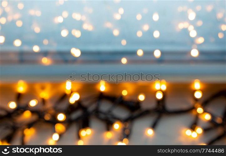 christmas, holidays and illumination concept - blurred electric garland lights on window sill. blurred electric garland lights on window sill