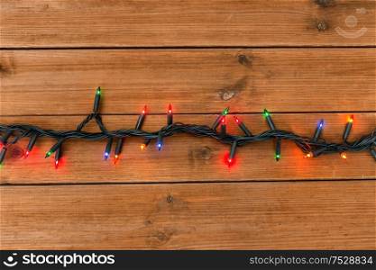 christmas, holidays and illumination concept - electric garland lights on wooden background. christmas garland lights on wooden background