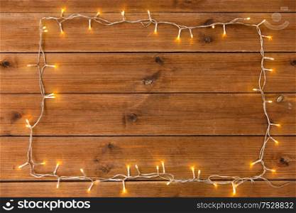 christmas, holidays and illumination concept - frame of electric garland lights on wooden background. frame of garland lights on wooden background