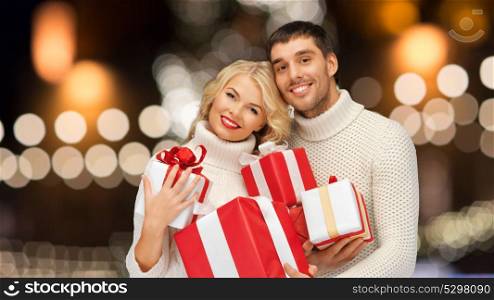 christmas, holidays and new year concept - happy family couple in sweaters holding gifts or presents over lights background. happy couple in sweaters holding christmas gifts