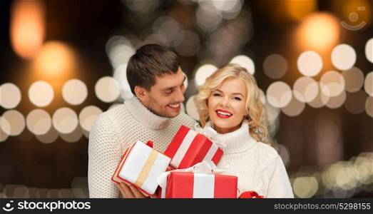 christmas, holidays and new year concept - happy family couple in sweaters holding gifts or presents over lights background. happy couple in sweaters holding christmas gifts