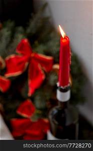 christmas, holidays and objects concept - close up of red candle burning in candlestick made of wine bottle at home. red christmas candle burning in wine bottle