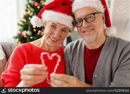 christmas, holidays and people concept - close up of happy smiling senior couple in santa hats with candy canes at home. close up of happy senior couple at christmas