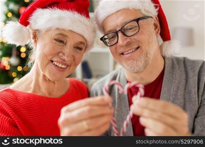 christmas, holidays and people concept - close up of happy smiling senior couple in santa hats with candy canes at home. close up of happy senior couple at christmas