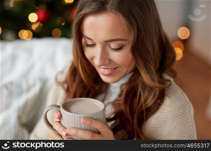 christmas, holidays and people concept - close up of happy young woman with cup of coffee or cocoa drink at home