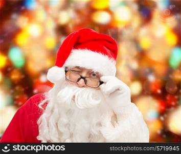 christmas, holidays and people concept - close up of santa claus in glasses winking over red lights background