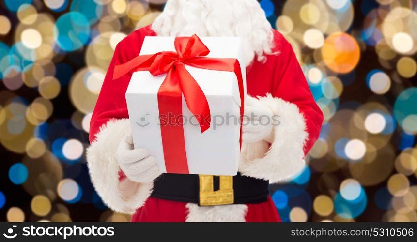 christmas, holidays and people concept - close up of santa claus with gift box over lights background. close up of santa claus with christmas gift