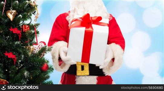 christmas, holidays and people concept - close up of santa claus with gift box and tree over blue lights background