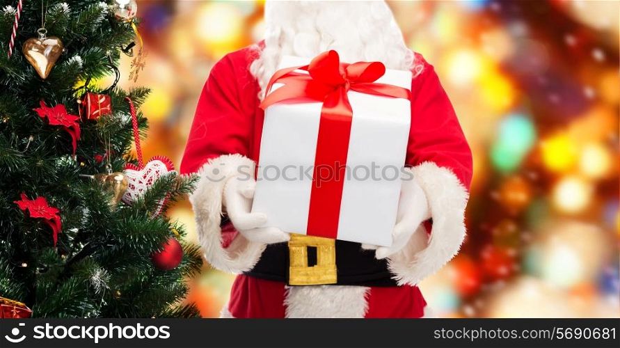 christmas, holidays and people concept - close up of santa claus with gift box and tree over red lights background