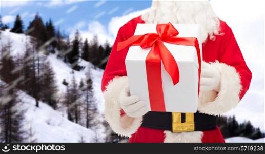 christmas, holidays and people concept - close up of santa claus with gift box over snowy mountains