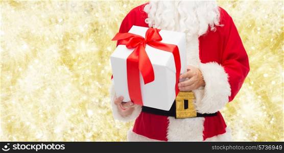 christmas, holidays and people concept - close up of santa claus with gift box over yellow lights background