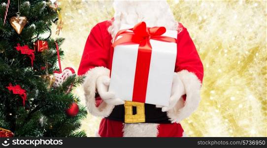 christmas, holidays and people concept - close up of santa claus with gift box and tree over yellow lights background