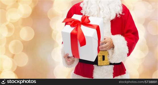 christmas, holidays and people concept - close up of santa claus with gift box over beige lights background