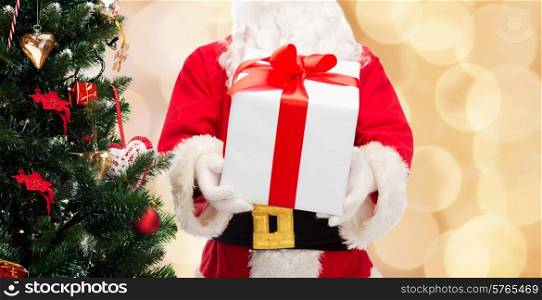 christmas, holidays and people concept - close up of santa claus with gift box and tree over beige lights background