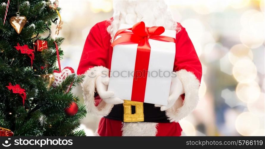 christmas, holidays and people concept - close up of santa claus with gift box and tree over lights background